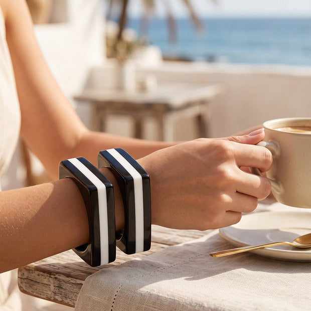 Woman wearing two black and white striped square resin bangles on wrist at a seaside cafe table