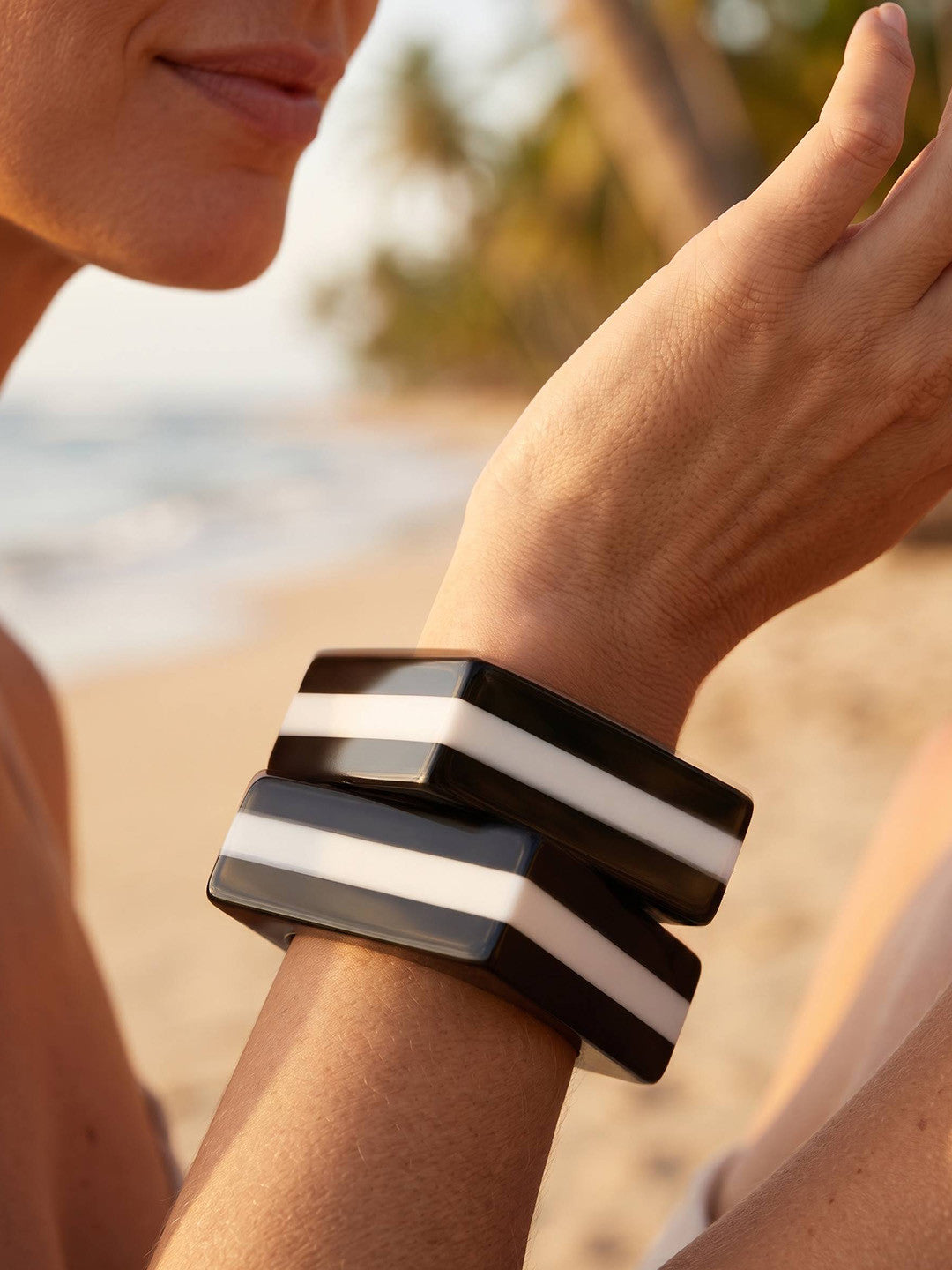 Close-up of woman's wrist stacked with two black and white striped square resin bangles on a beach