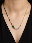 Model wearing gold-plated emerald green CZ mangalsutra over black deep-neck top