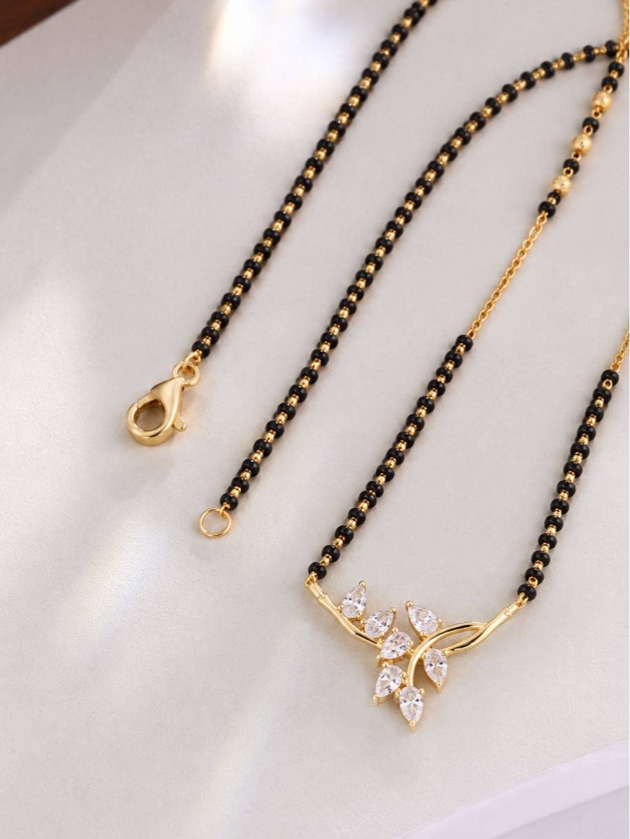 Close-up of CZ leaf pendant and lobster clasp closure of gold-plated mangalsutra laid flat