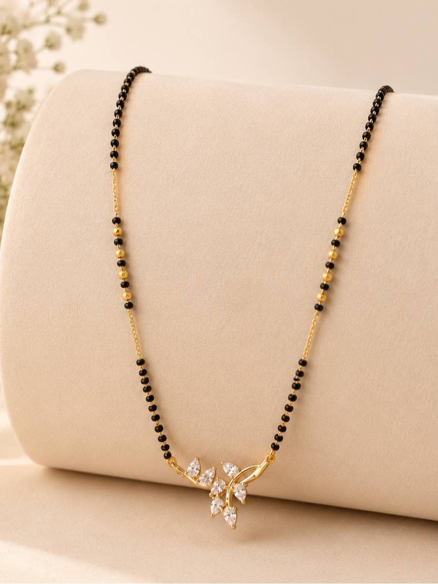 Full-length view of gold-plated CZ leaf mangalsutra draped on a beige display cushion