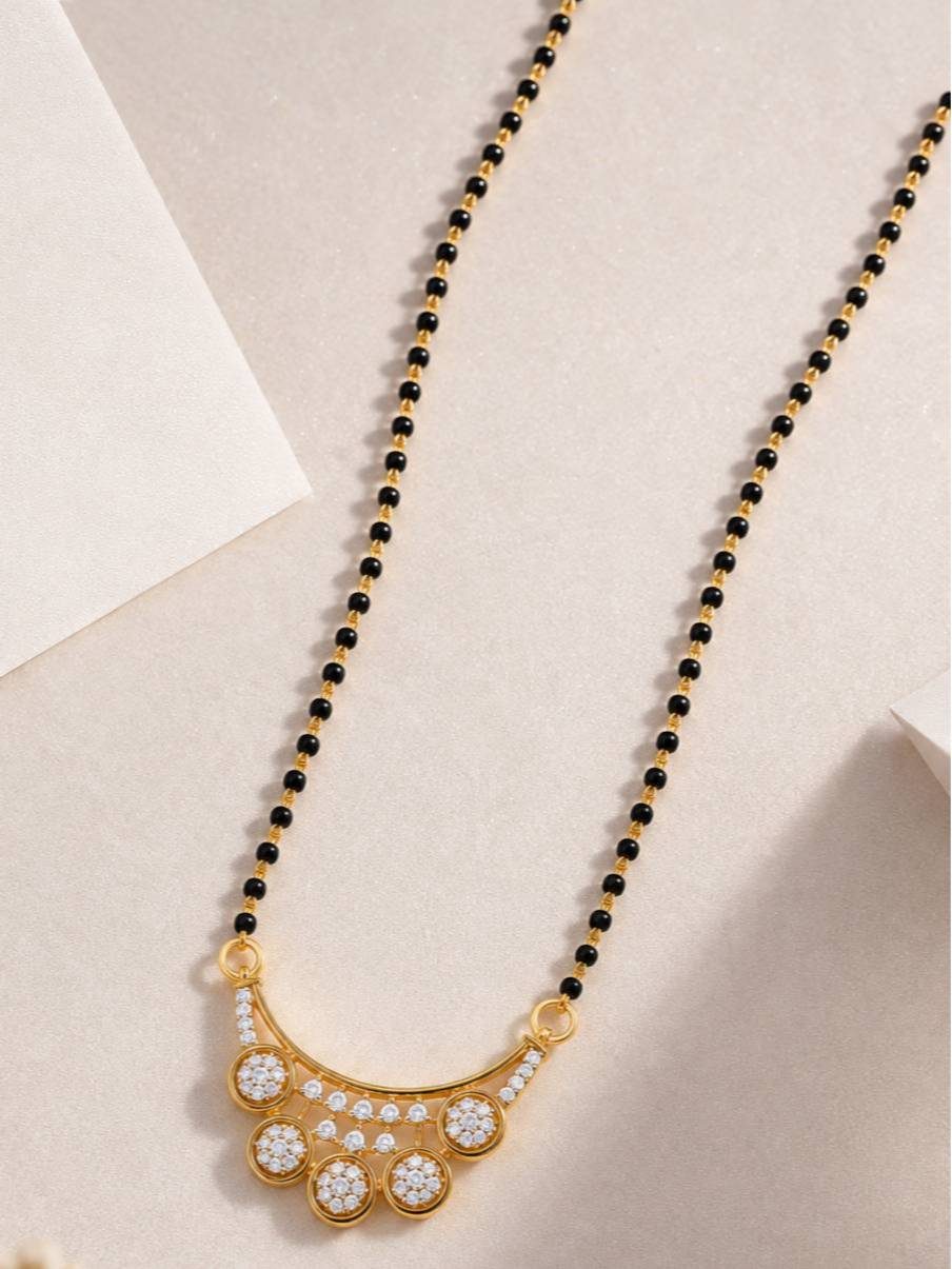 Black bead gold-plated mangalsutra with CZ fan pendant on a beige surface from above