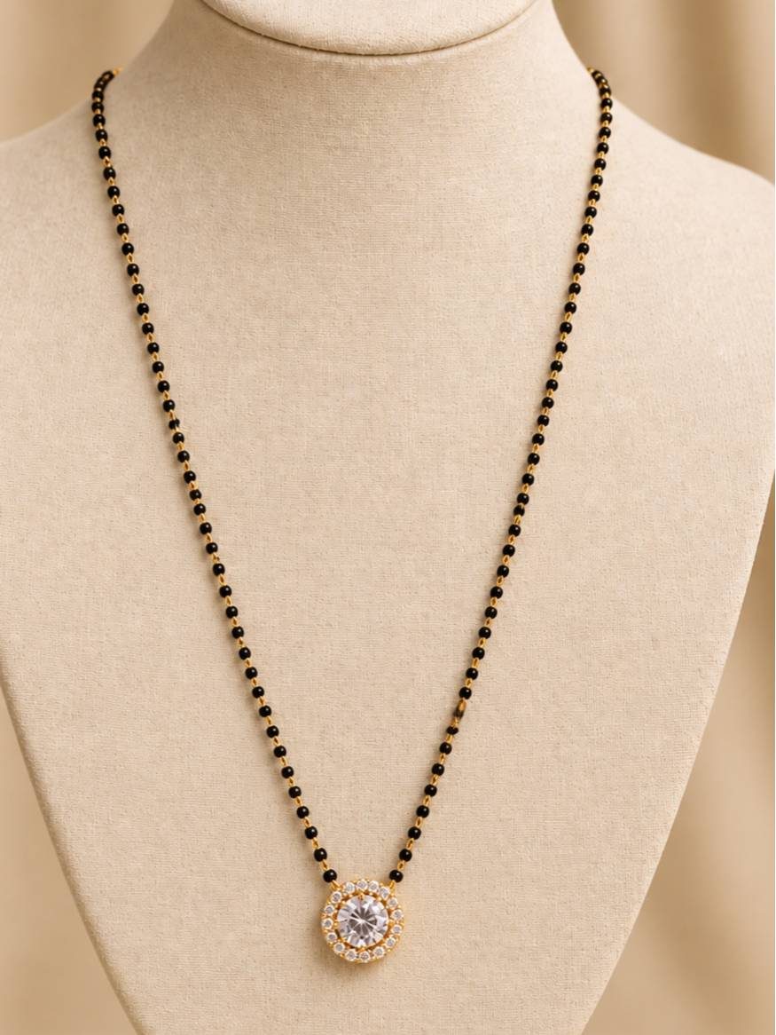Gold-plated CZ solitaire mangalsutra with black bead chain displayed on a cream jewellery bust