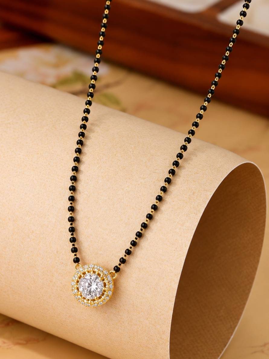 Close-up of round CZ halo pendant on gold-plated mangalsutra resting on a rolled paper surface