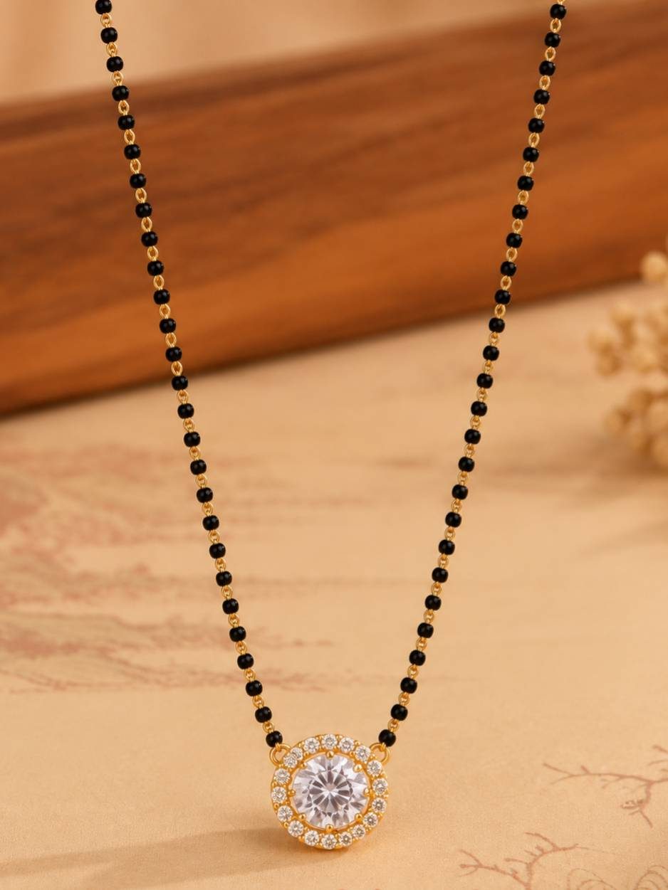 Gold-plated black bead mangalsutra with CZ solitaire pendant laid flat on a printed fabric surface
