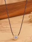 Gold-plated black bead mangalsutra with CZ solitaire pendant laid flat on a printed fabric surface
