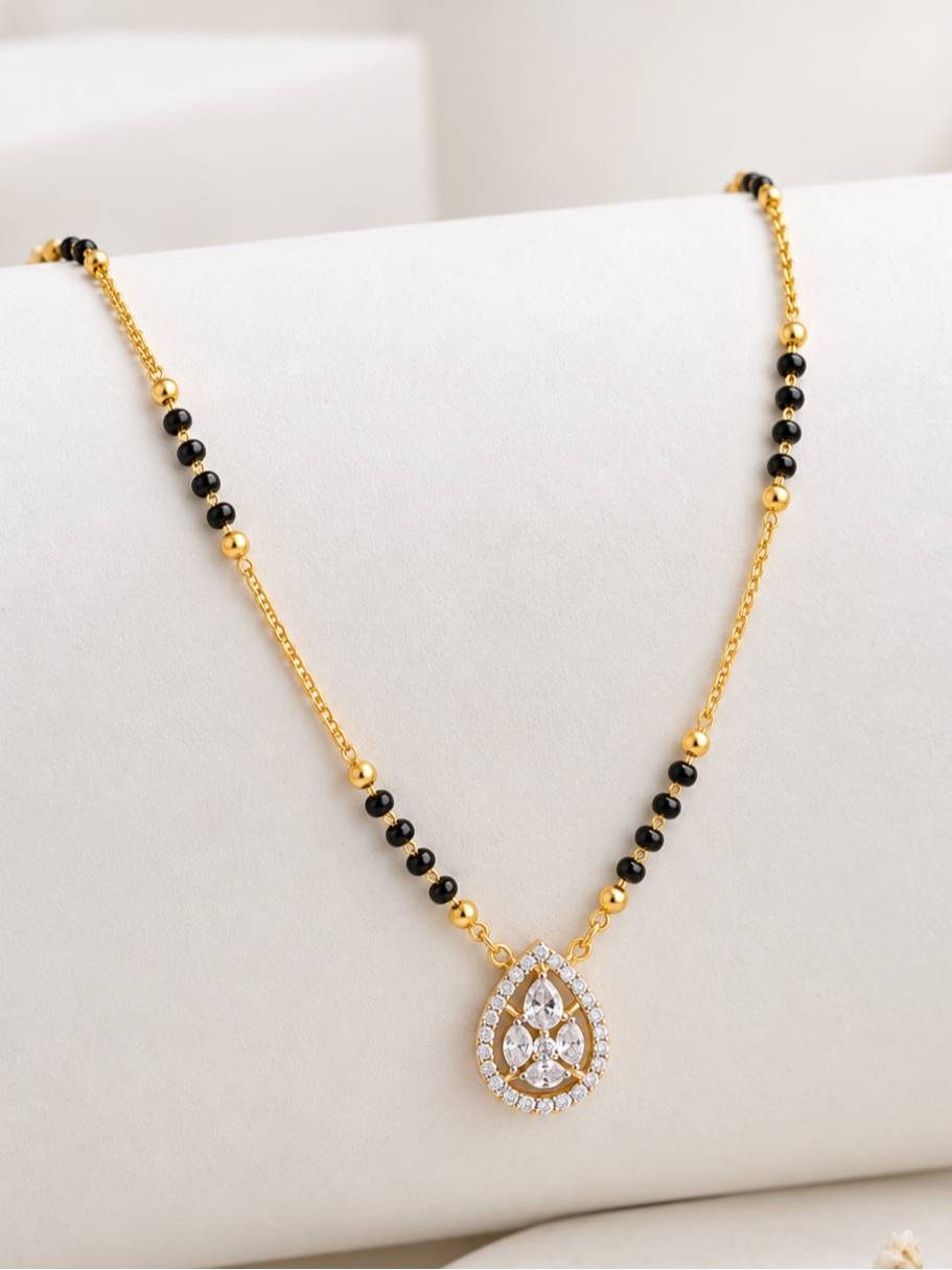 Close-up of gold-plated mangalsutra with cubic zirconia teardrop pendant on white surface