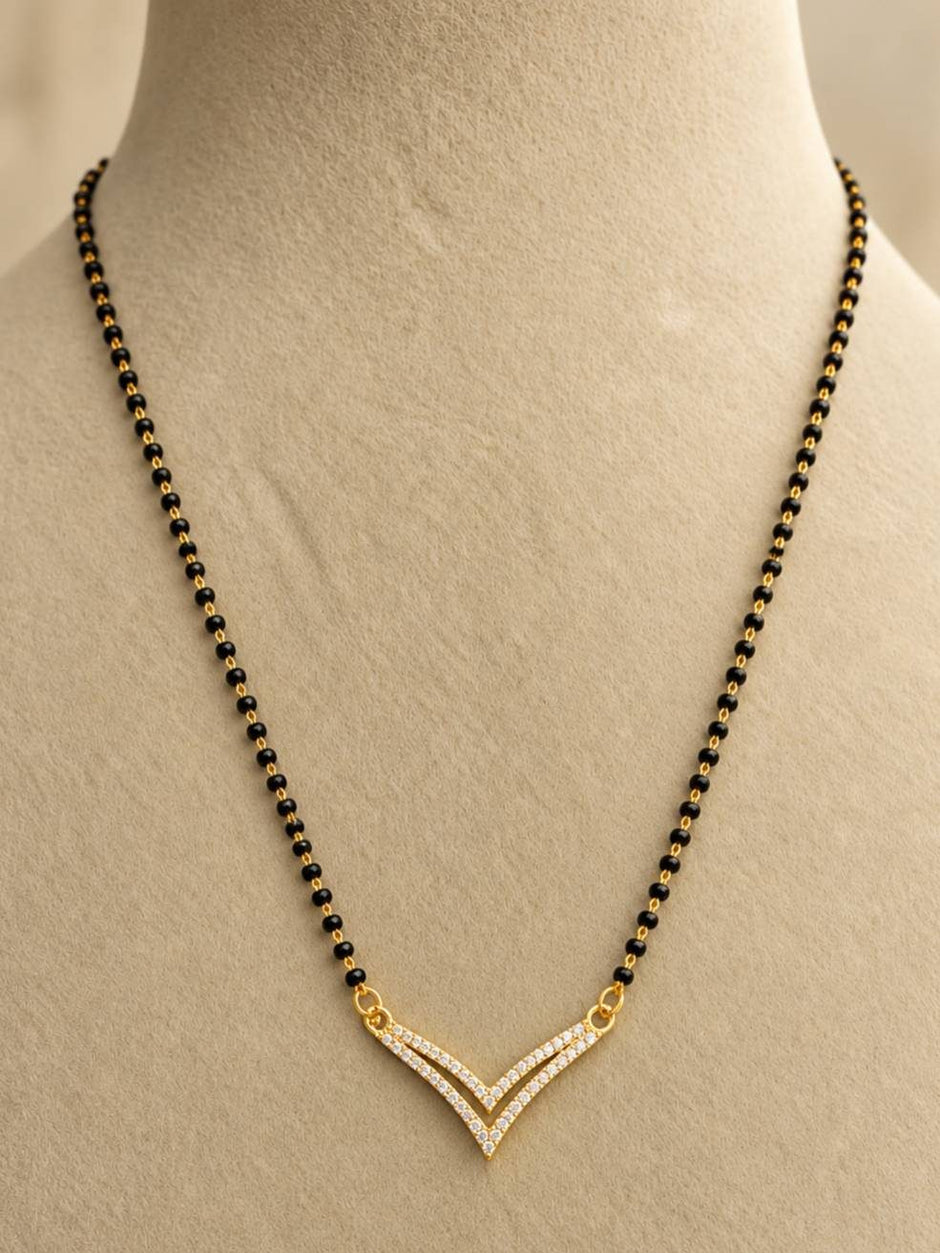 Gold-plated double V CZ mangalsutra displayed on a cream jewellery bust, showing full black bead chain