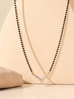 CZ chevron mangalsutra pendant hanging on a long black bead chain against a peach display stand