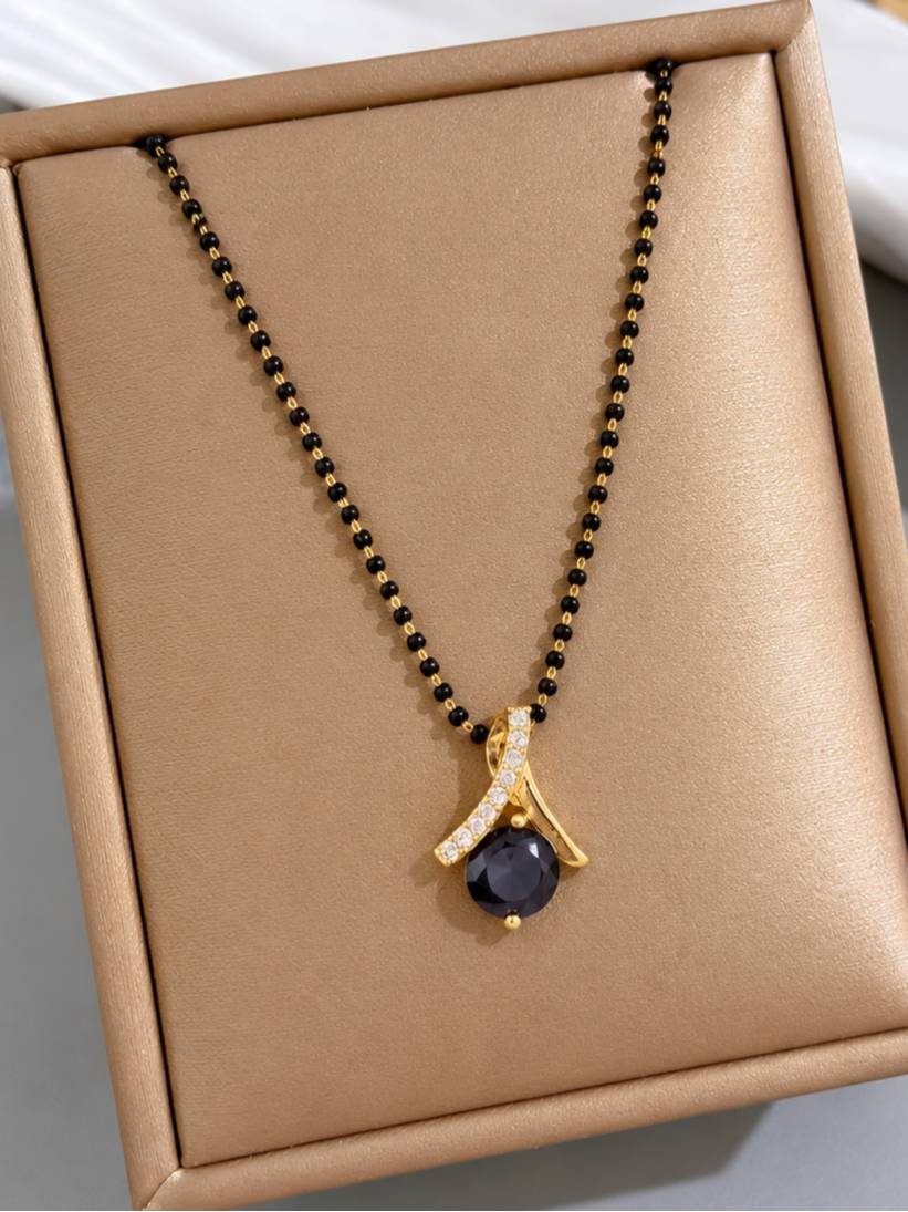 Gold-plated black bead mangalsutra with black stone and CZ pendant displayed in a tan jewellery box