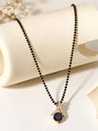 Full length view of black bead mangalsutra with gold crossover pendant resting on a cream cylindrical display prop