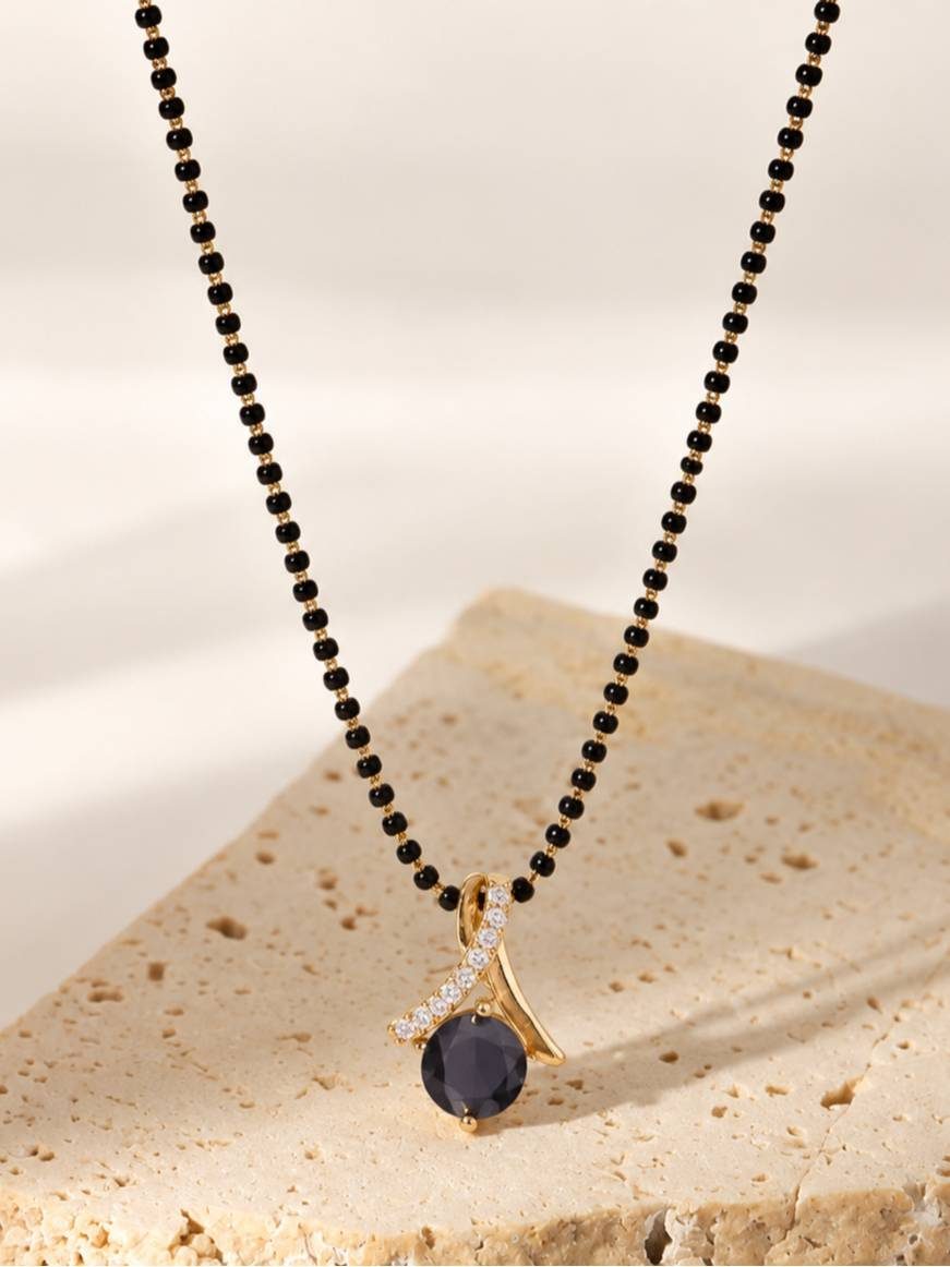 Black bead gold-plated mangalsutra with round black stone pendant laid on a textured stone surface