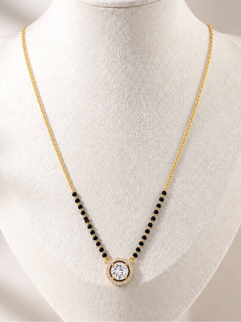 Gold-plated black bead mangalsutra with round CZ halo pendant displayed on a white jewellery bust