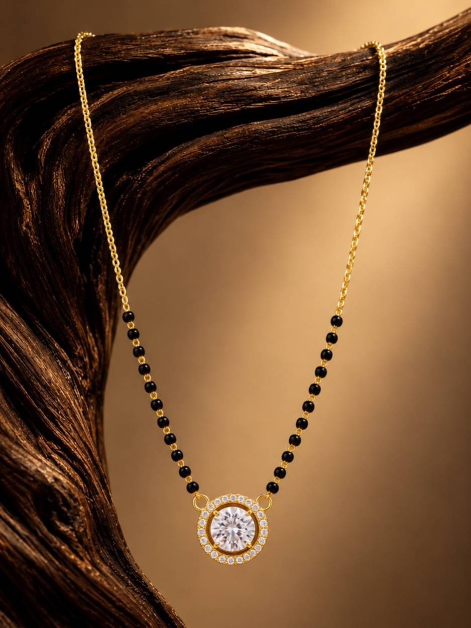 Black bead mangalsutra with solitaire CZ pendant draped over a dark wooden branch against a warm gold background