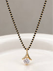 Black bead mangalsutra with gold-plated CZ solitaire pendant laid flat on a white curved surface