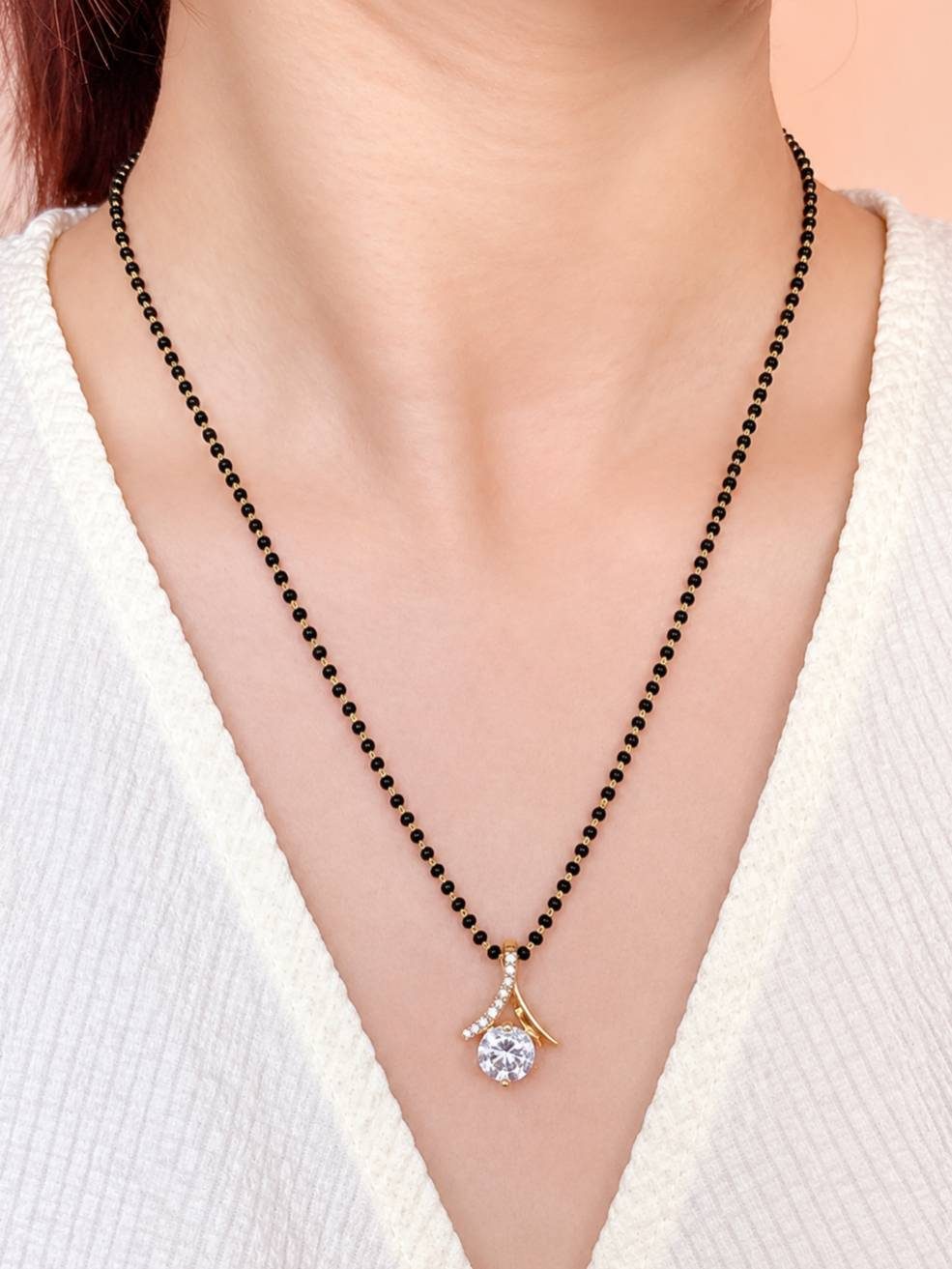 Model wearing gold-plated black bead mangalsutra with CZ pendant over a white ribbed top