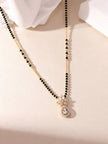 Flat lay of gold-plated mangalsutra with marquise CZ flower and teardrop halo pendant on cream surface
