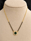 Gold-plated mangalsutra with emerald green CZ halo pendant displayed on a cream jewellery bust
