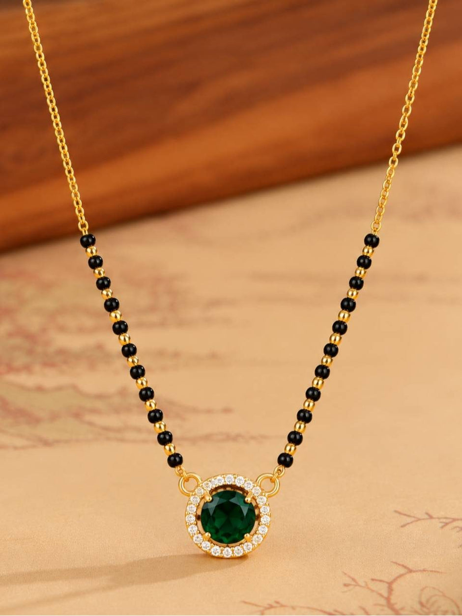 Close-up of green cubic zirconia mangalsutra pendant with white CZ halo and black bead chain on warm background
