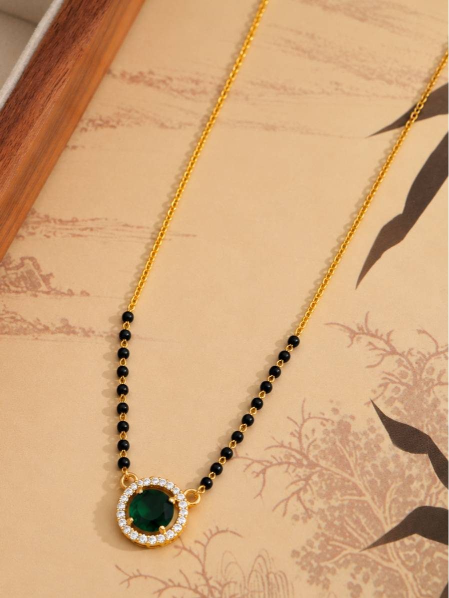 Full-length view of black bead and gold-tone mangalsutra chain with round green pendant laid flat on decorative paper