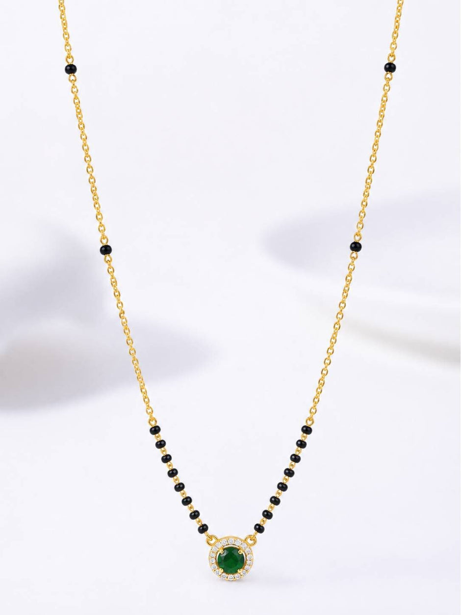 Full view of gold-plated black bead mangalsutra with round emerald CZ pendant against white background