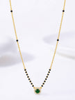 Full view of gold-plated black bead mangalsutra with round emerald CZ pendant against white background