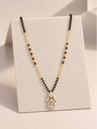Gold-plated mangalsutra with black beads and rose pink CZ pendant displayed on a cream jewellery stand