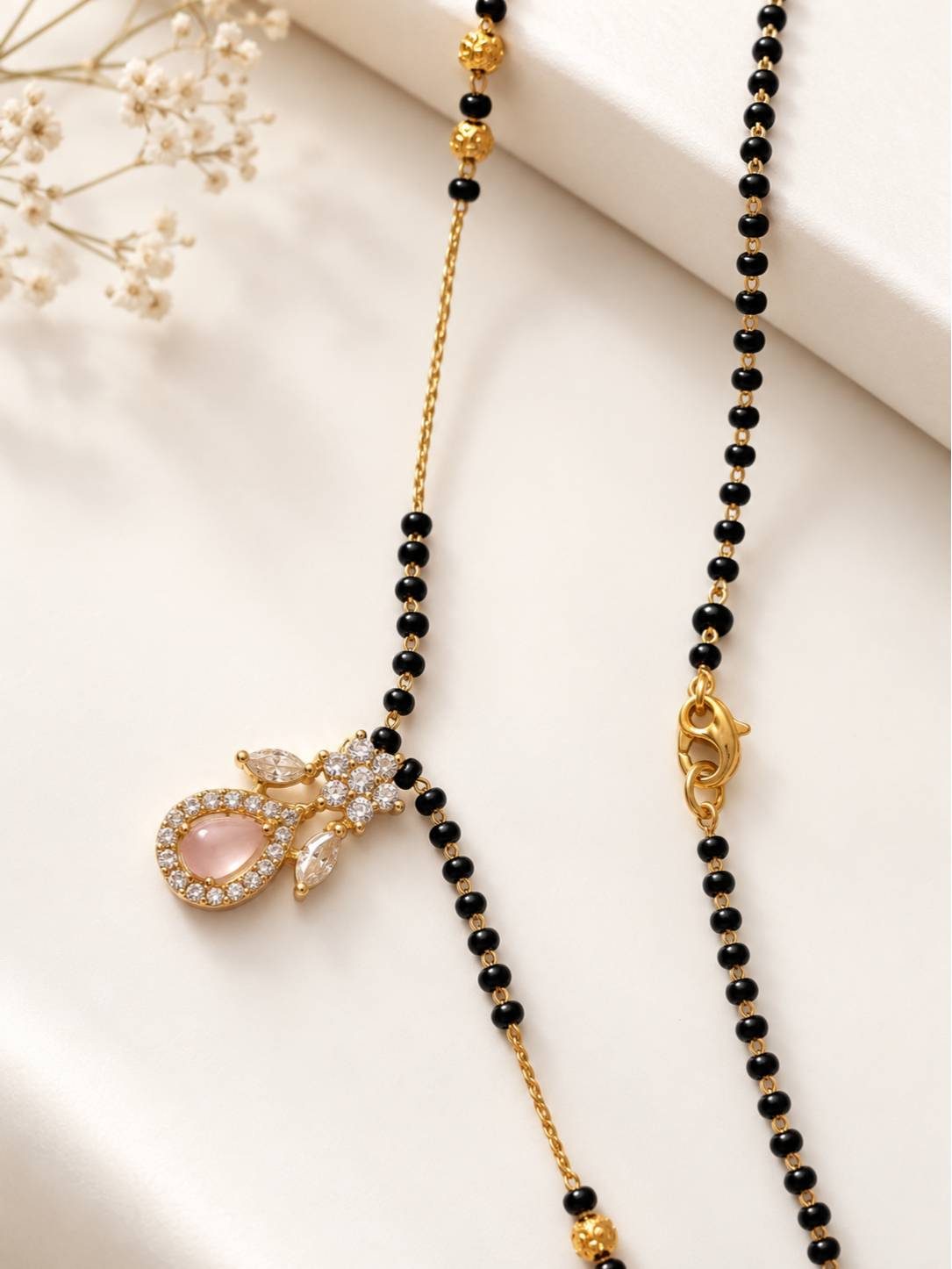 Close-up of CZ pendant and lobster clasp of gold-plated black bead mangalsutra on white surface