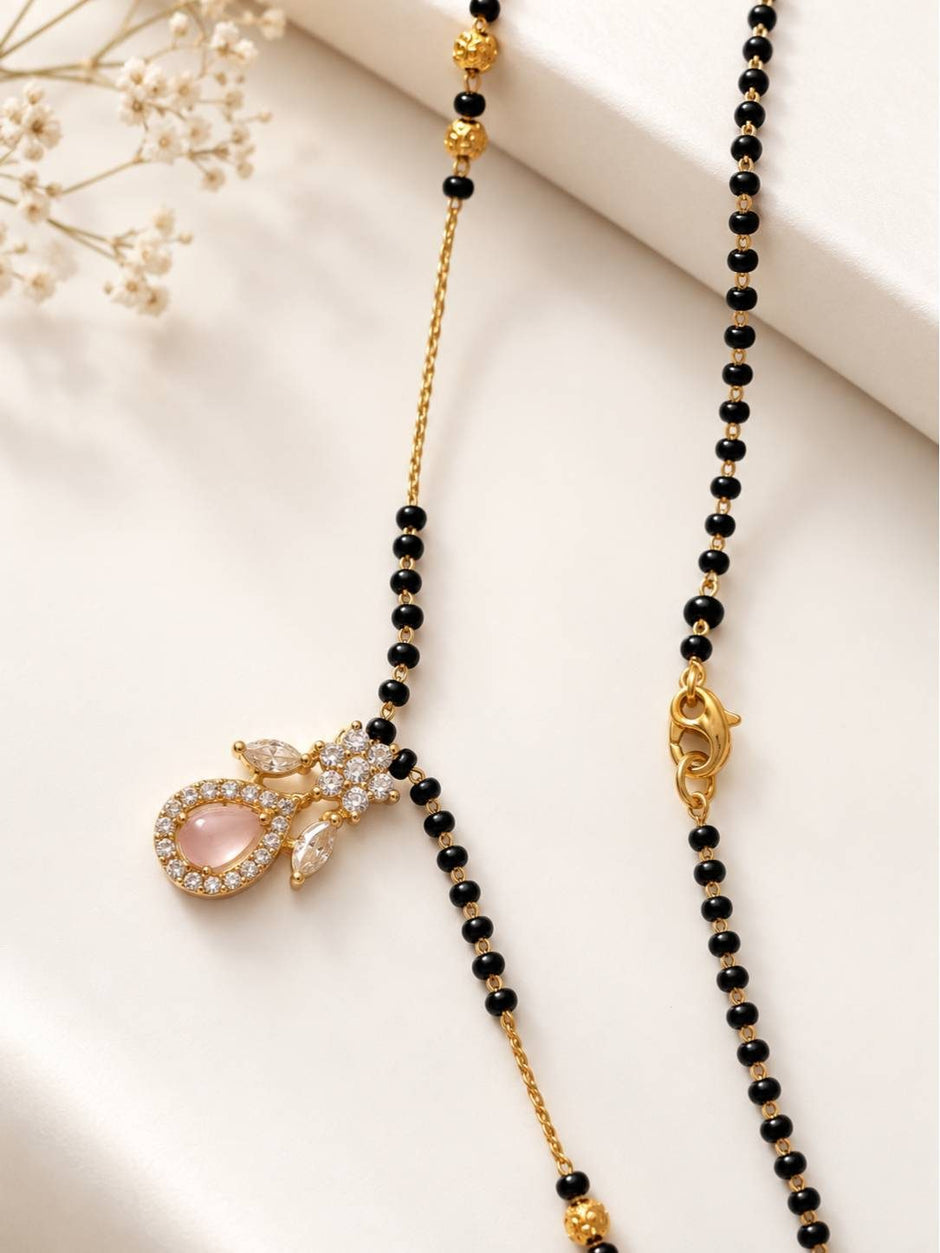 Close-up of CZ pendant and lobster clasp of gold-plated black bead mangalsutra on white surface