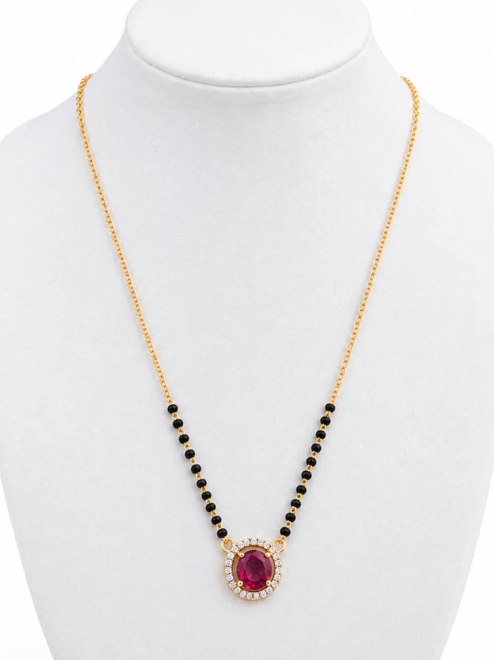 Gold-plated mangalsutra with ruby CZ halo pendant and black bead chain on white jewellery bust