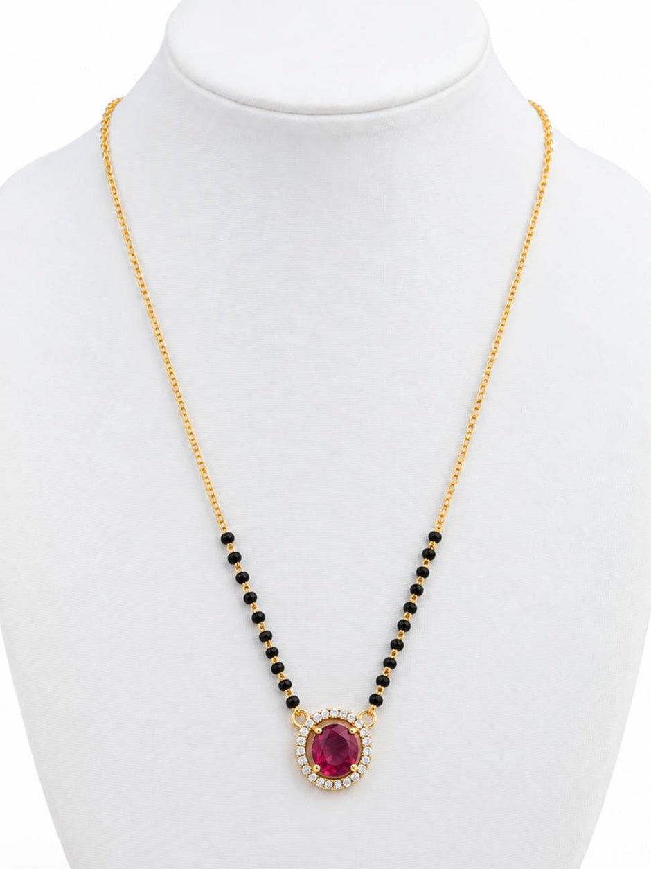 Gold-plated mangalsutra with ruby CZ halo pendant and black bead chain on white jewellery bust