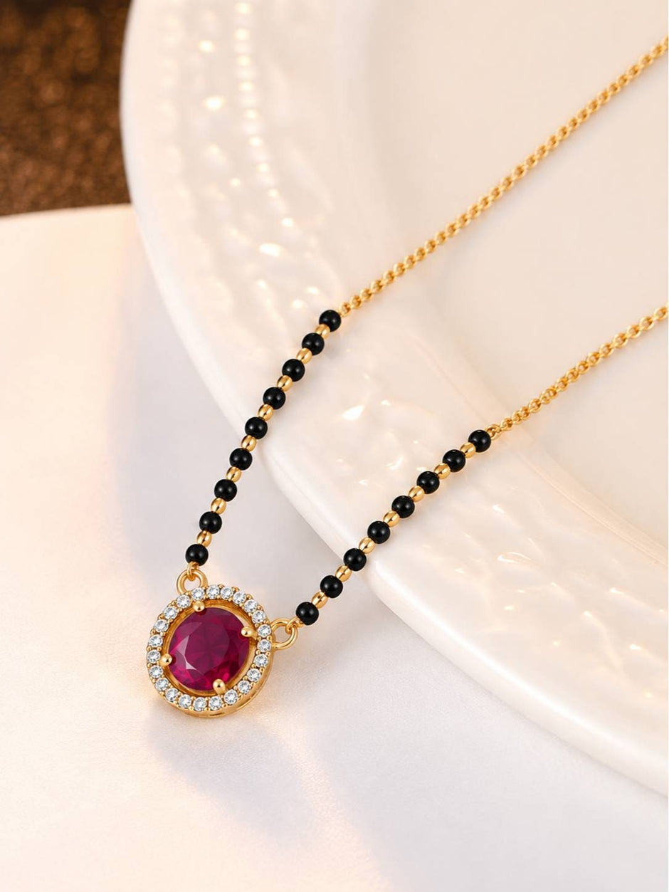 Close-up of gold-plated fuchsia CZ pendant with white CZ halo and black bead chain on white dish