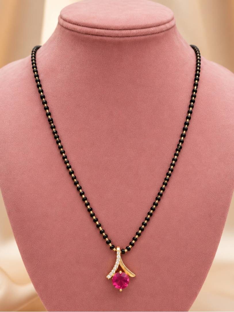 Gold-plated mangalsutra with fuchsia stone pendant displayed on a pink velvet jewellery bust