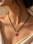 Gold-plated black bead mangalsutra with fuchsia pendant worn around a woman's neck over a white satin outfit