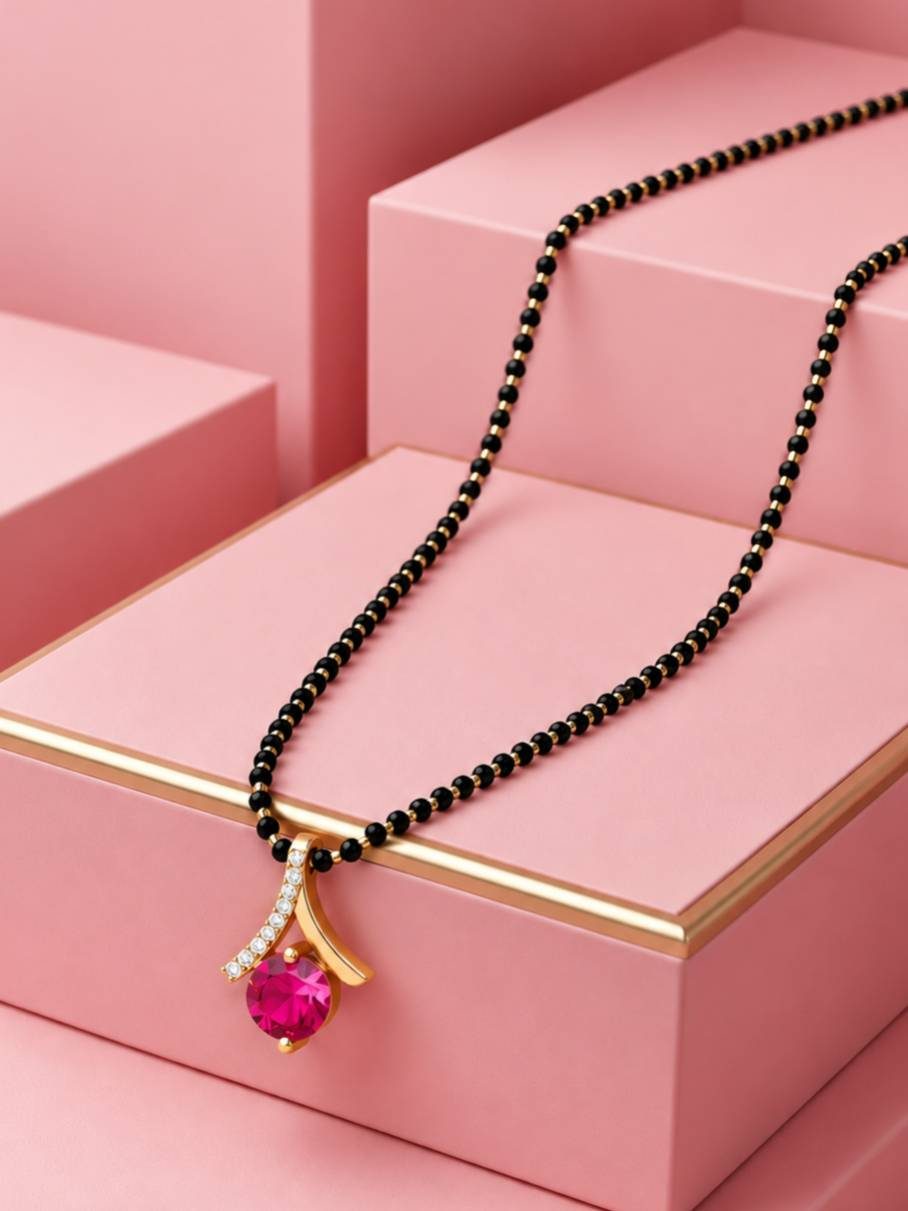 Mangalsutra with ruby red stone pendant laid flat across stacked pink geometric display blocks