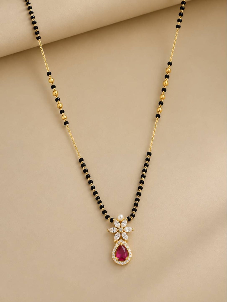 Full-length view of black bead gold mangalsutra with fuchsia CZ drop pendant on beige fabric
