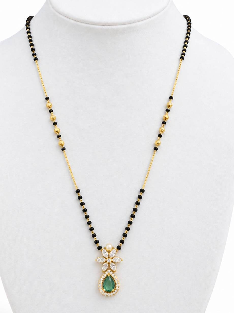 Gold-plated mangalsutra with black beads and emerald green teardrop pendant displayed on white jewellery bust