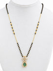 Gold-plated mangalsutra with black beads and emerald green teardrop pendant displayed on white jewellery bust