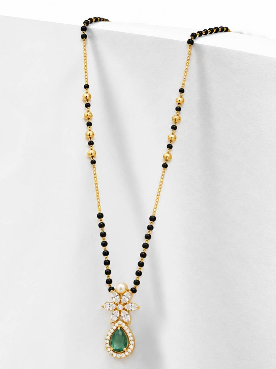 Side-angle view of gold-plated mangalsutra with black beads and emerald CZ pendant against white background