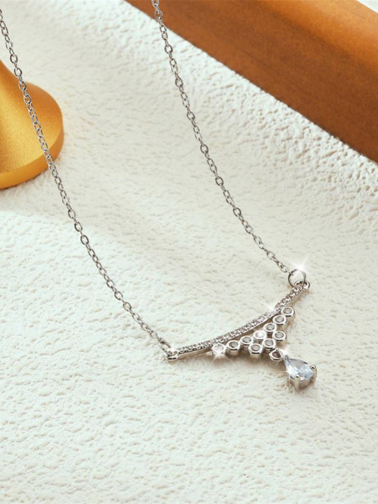 Side-angle view of silver cubic zirconia drop necklace laid flat on a white textured surface