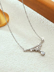 Side-angle view of silver cubic zirconia drop necklace laid flat on a white textured surface