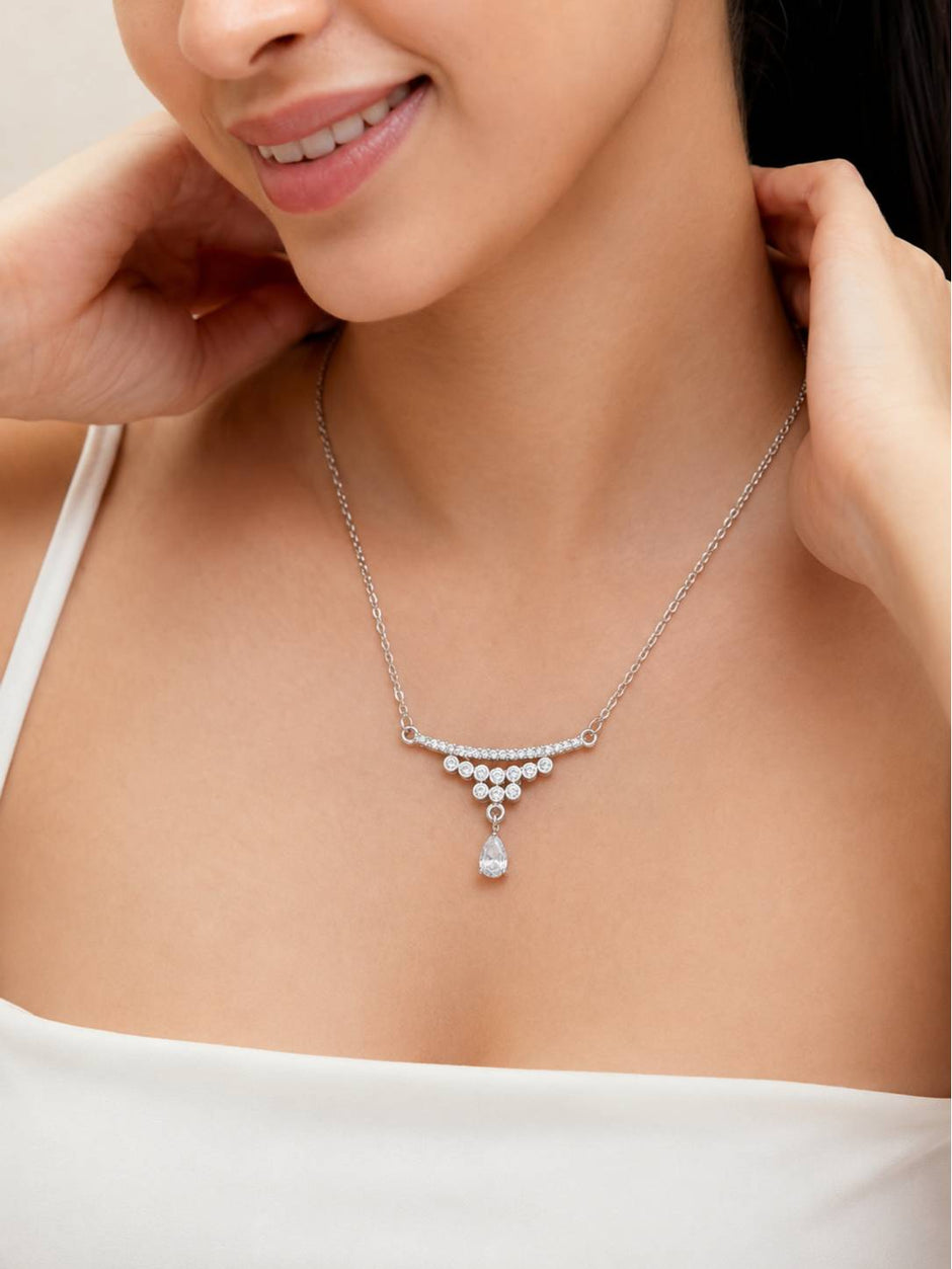 Woman wearing silver cubic zirconia teardrop drop necklace on a white outfit, smiling