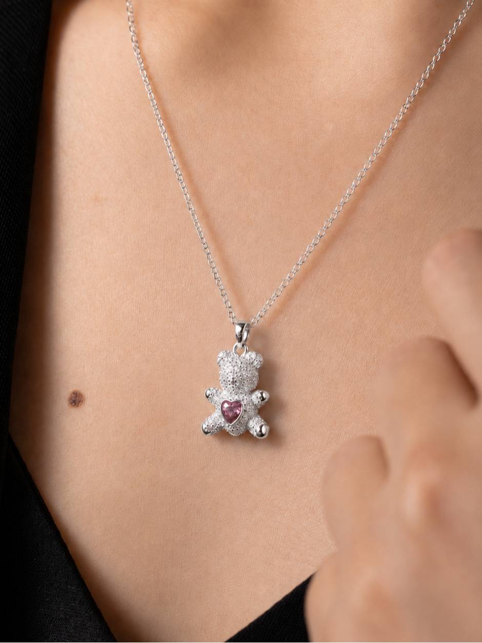 Model wearing silver teddy bear pendant necklace against bare collarbone with dark top