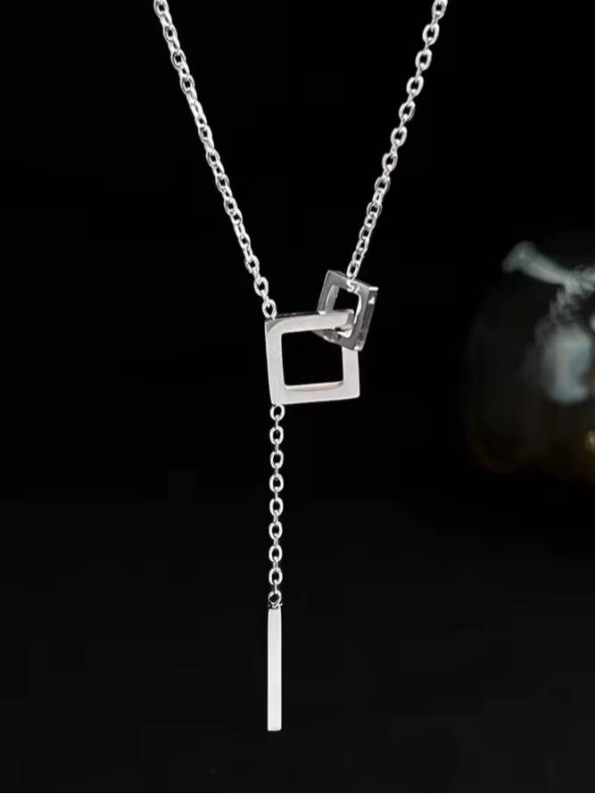 Silver-tone lariat necklace with two interlocked open squares and a slim bar drop hanging against a dark background