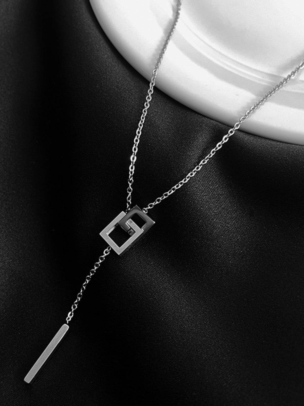 Silver lariat necklace draped on black satin fabric showing interlocked square pendant and dangling bar