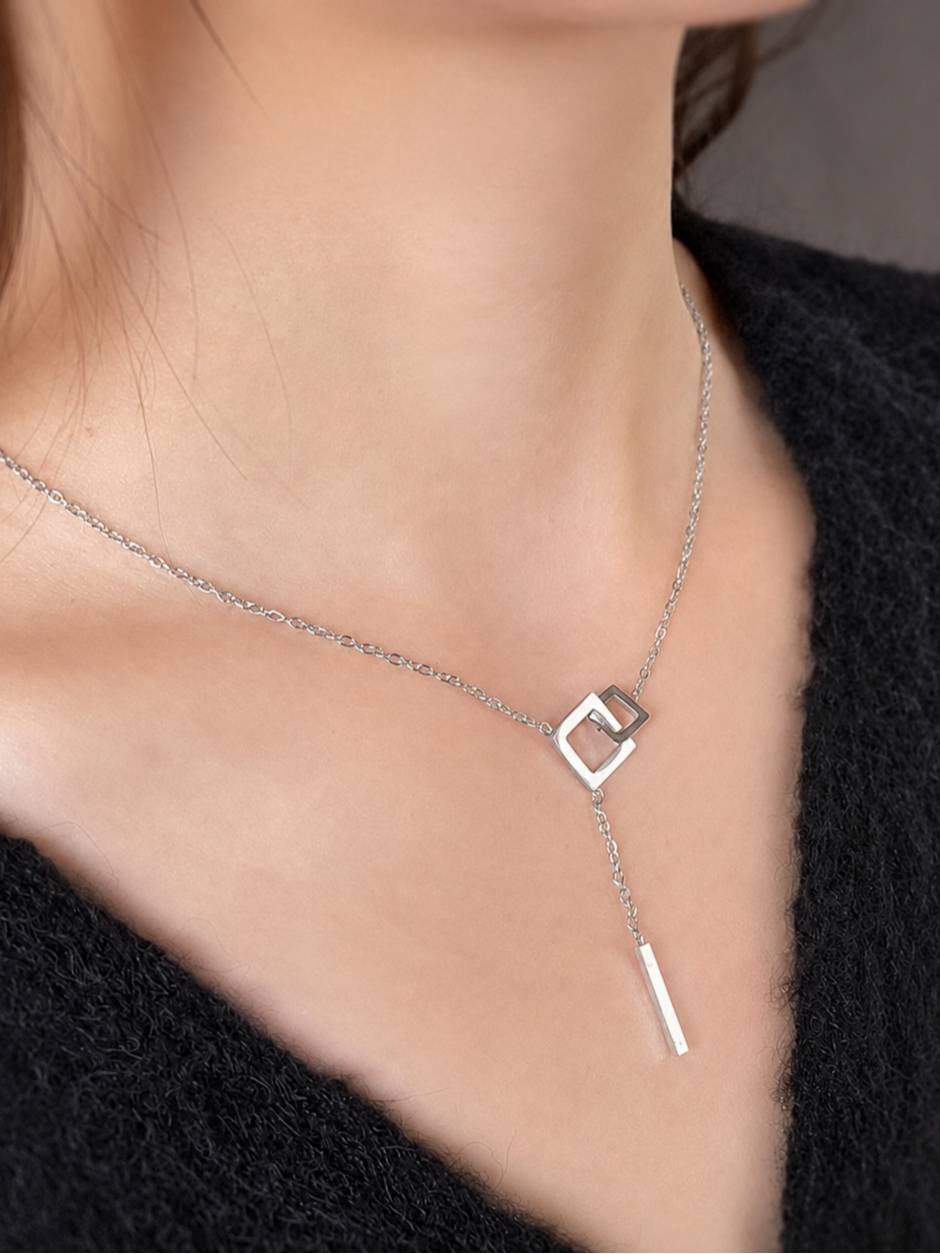 Silver lariat necklace worn on a model's neck over a black sweater, showing pendant and bar drop at décolletage