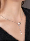 Silver lariat necklace worn on a model's neck over a black sweater, showing pendant and bar drop at décolletage