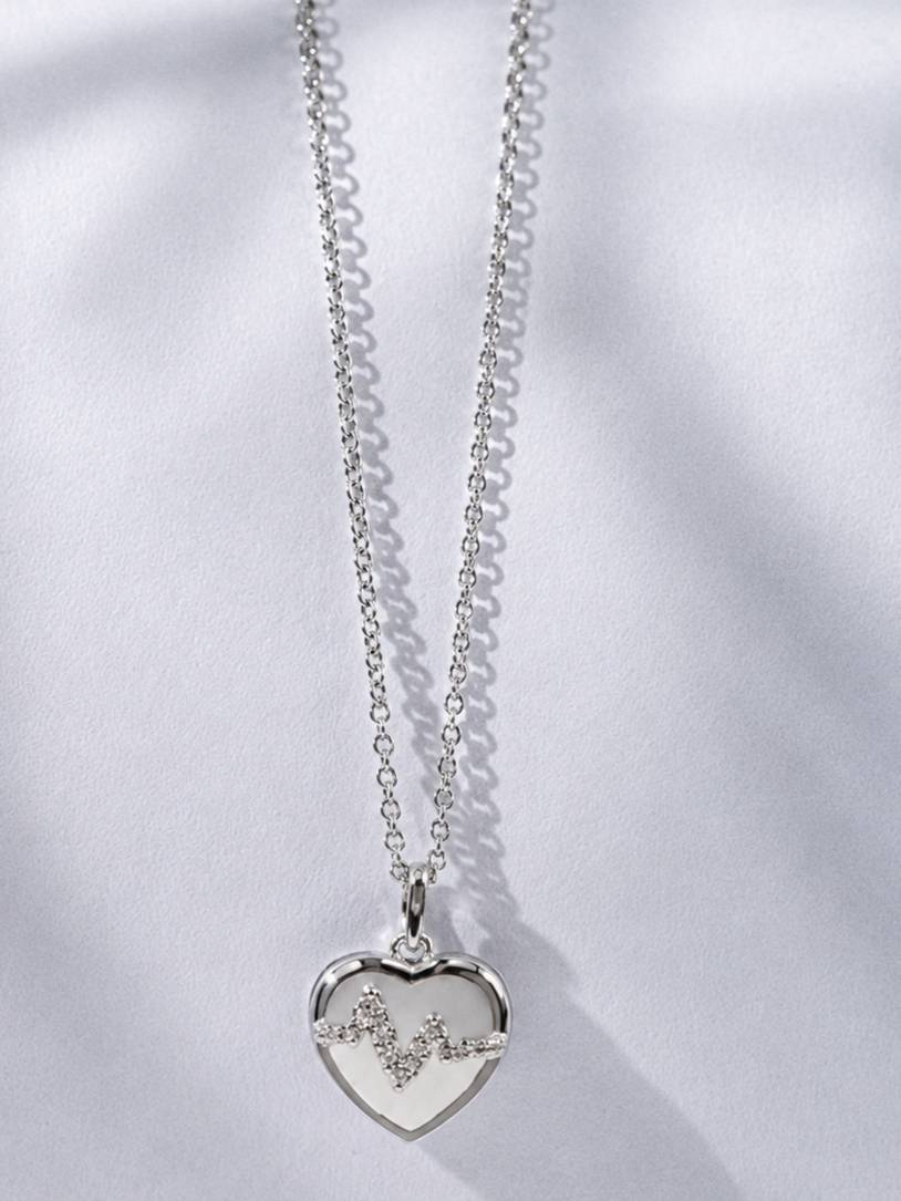 Front view of silver heart EKG pendant necklace on white fabric background