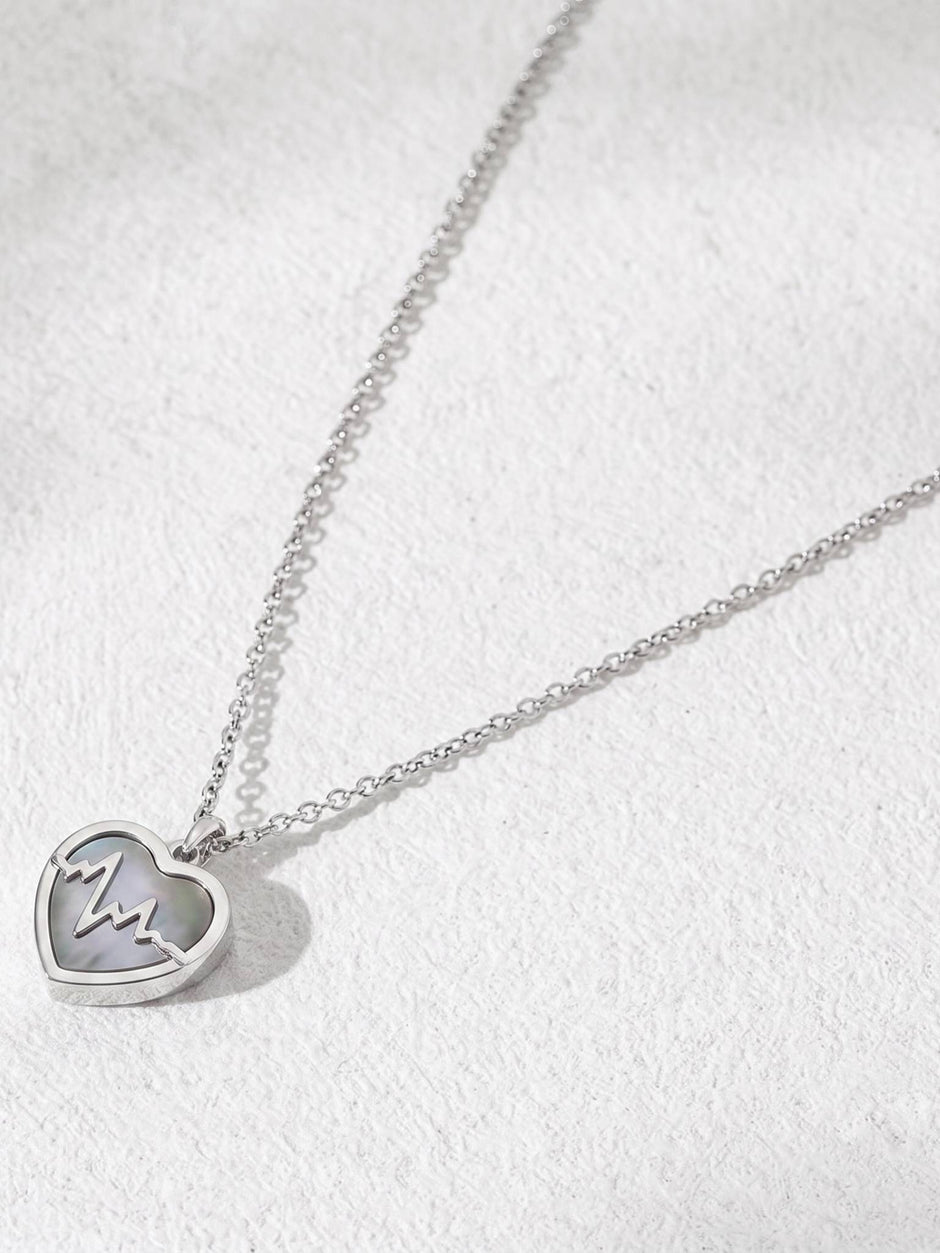 Angled flat-lay of silver heartbeat heart pendant necklace on textured white surface