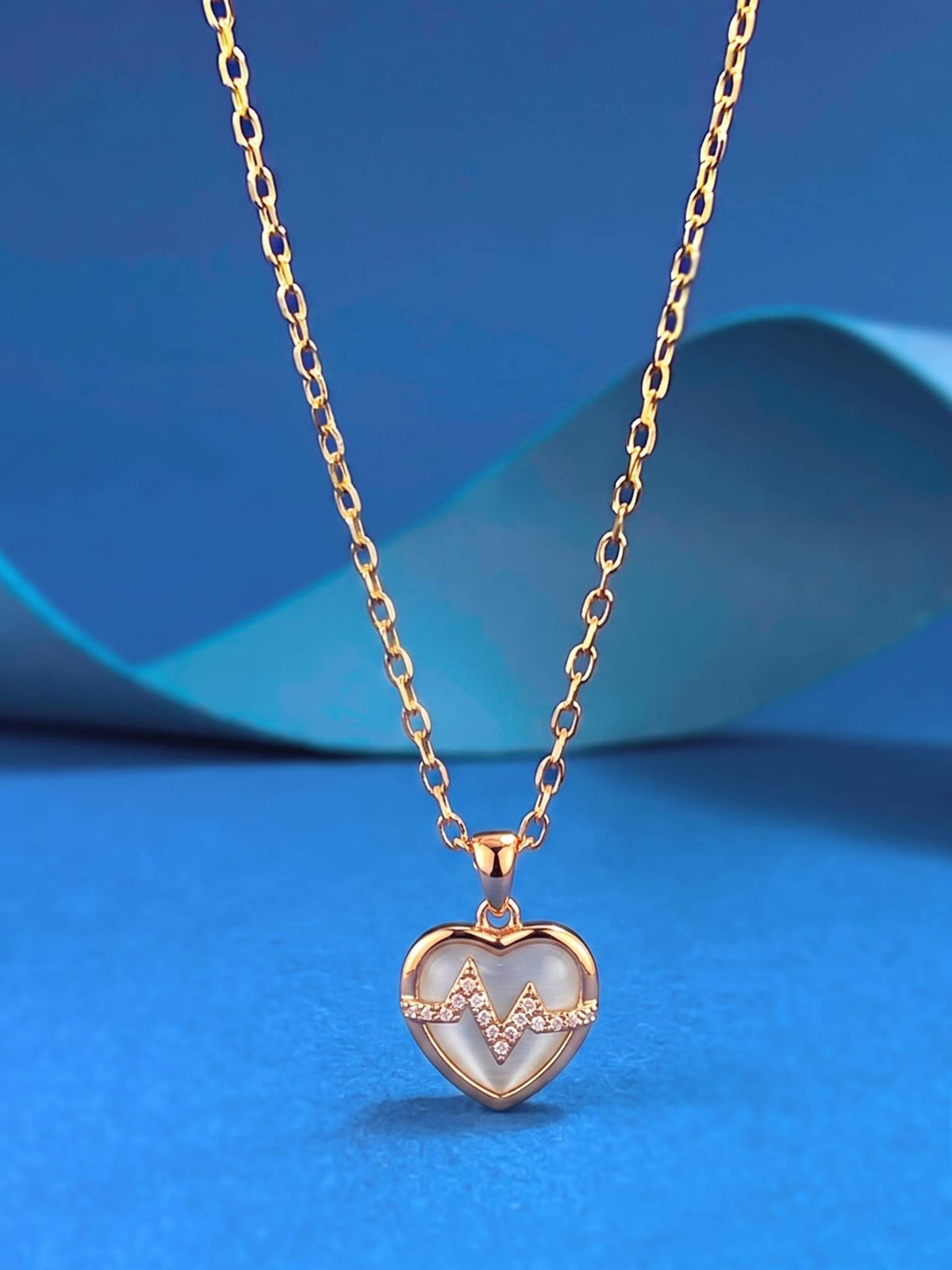 Heart heartbeat pendant necklace hanging against a blue background showing full cable chain
